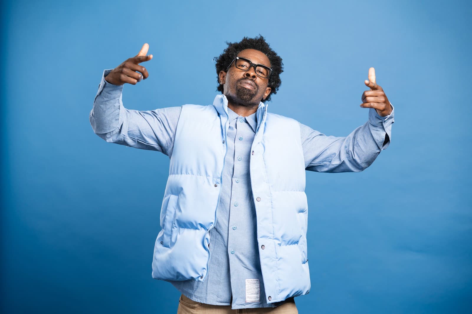 Stroy Moyd with both arms raised mid-joke, eyes closed, in a light blue vest.