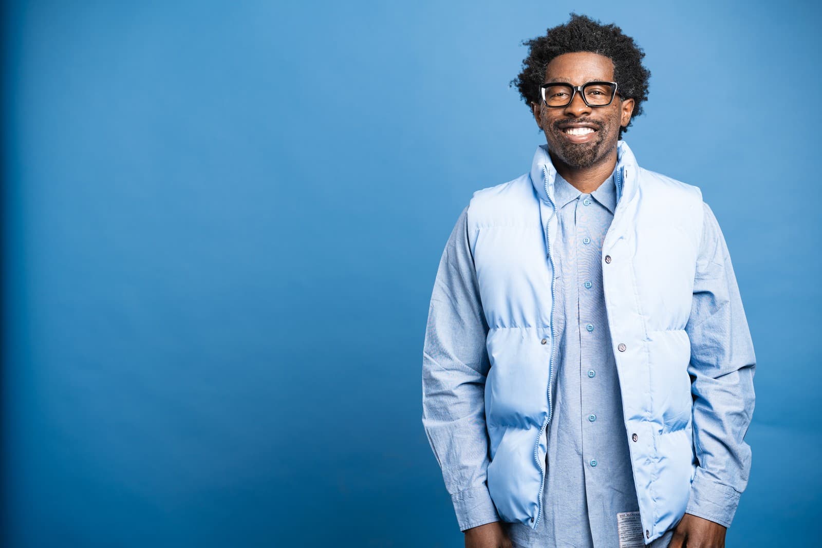Stroy Moyd smiling in a light blue puffer vest and black glasses.